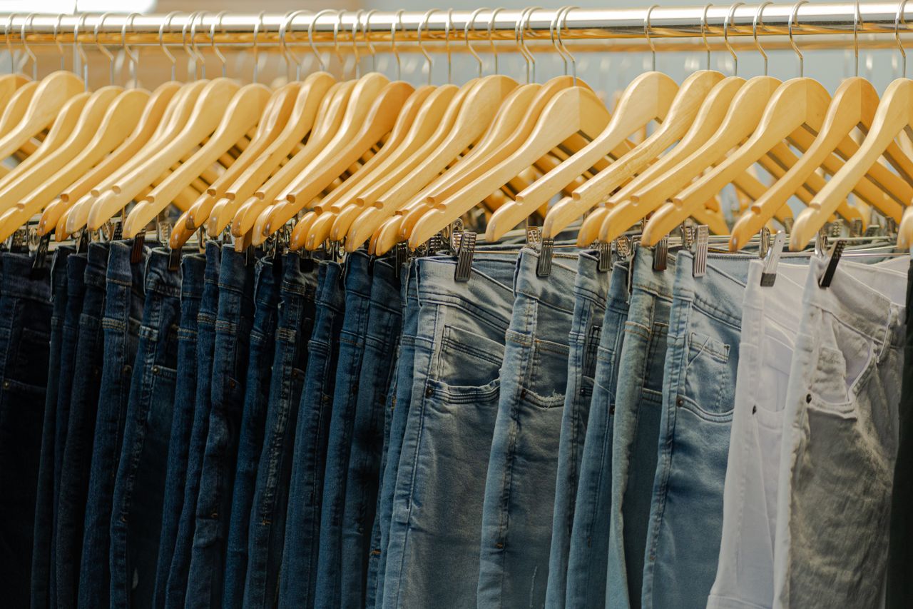 about-img Close-up of various denim jeans hanging on wooden hangers in a fashionable store.