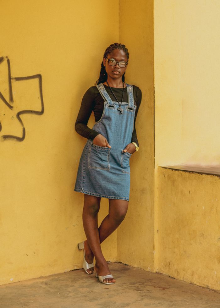 The Art of Drawing Readers In: Your attractive post title goes here Stylish woman in a denim dress poses confidently by a bright yellow wall.